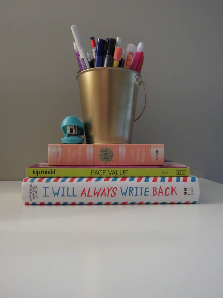 Books on my daughters Ikea desk with a gold cup holding pencils on top.