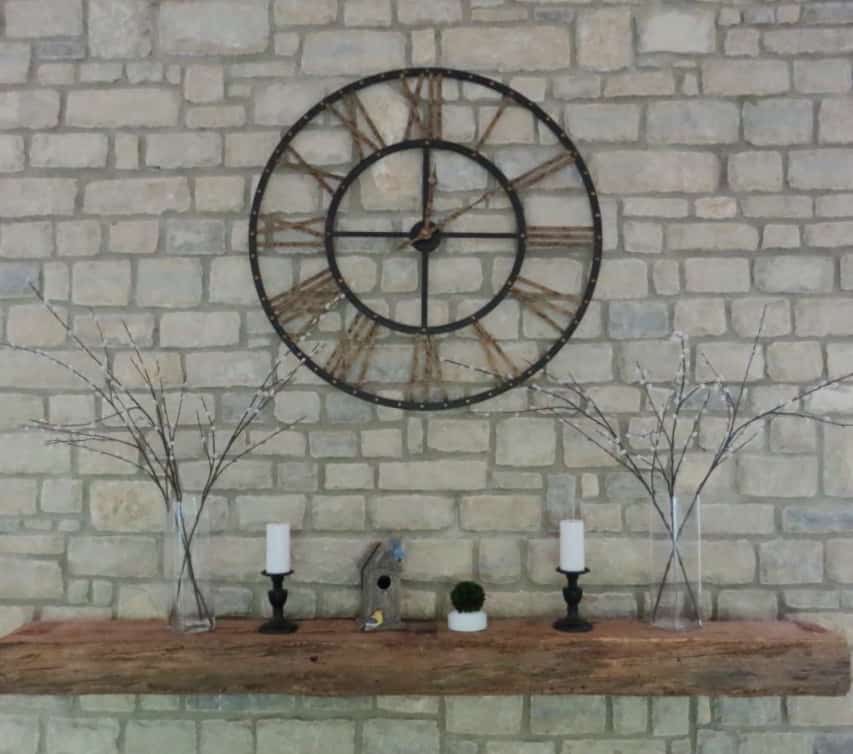 The clock hanging on my stone fireplace above a large wooden beam for a mantel.