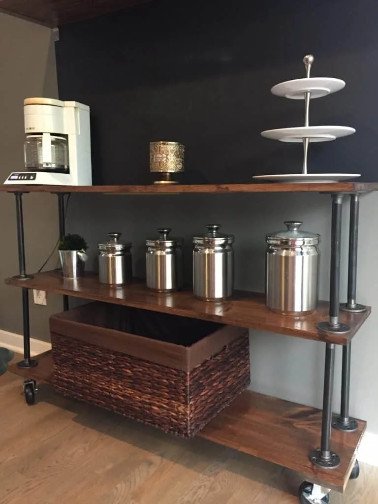 The finished industrial pipe shelves with silver canisters and a big brown basket on the bottom shelf.