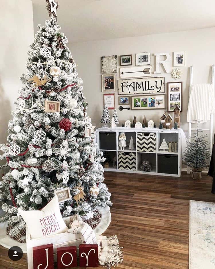 A flocked Christmas tree in a room with a gallery wall behind it.