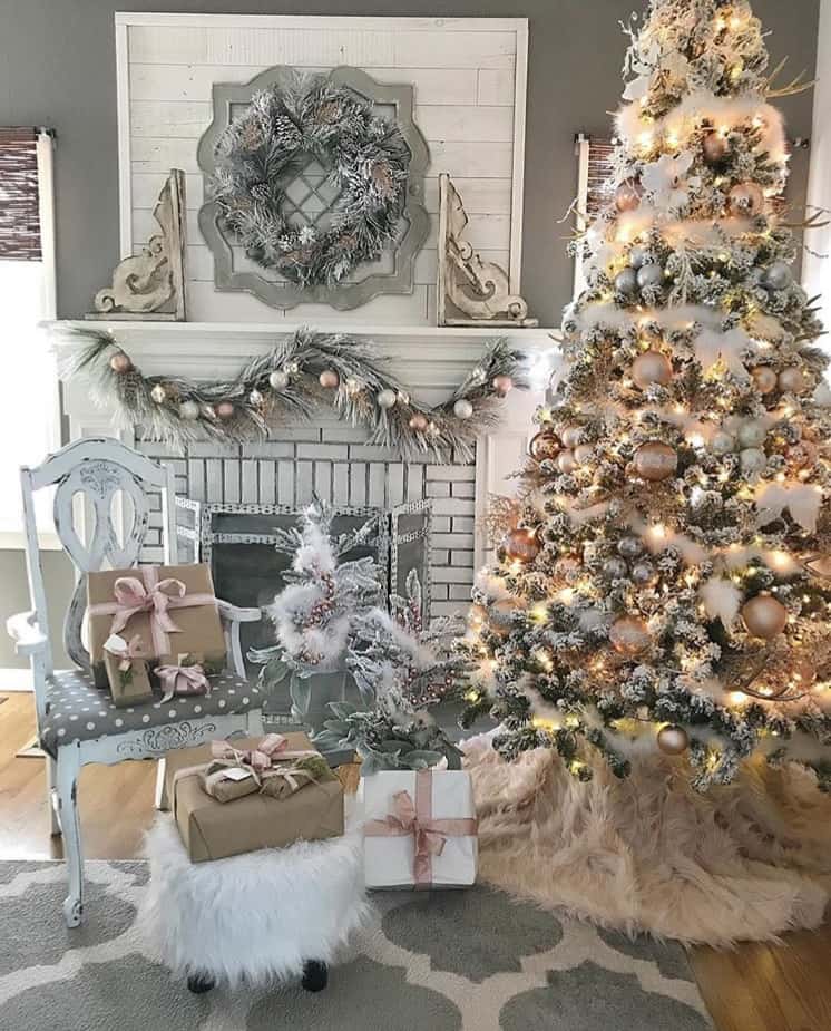 A flocked Christmas tree next to a fireplace and everything is decorated in muted tones.