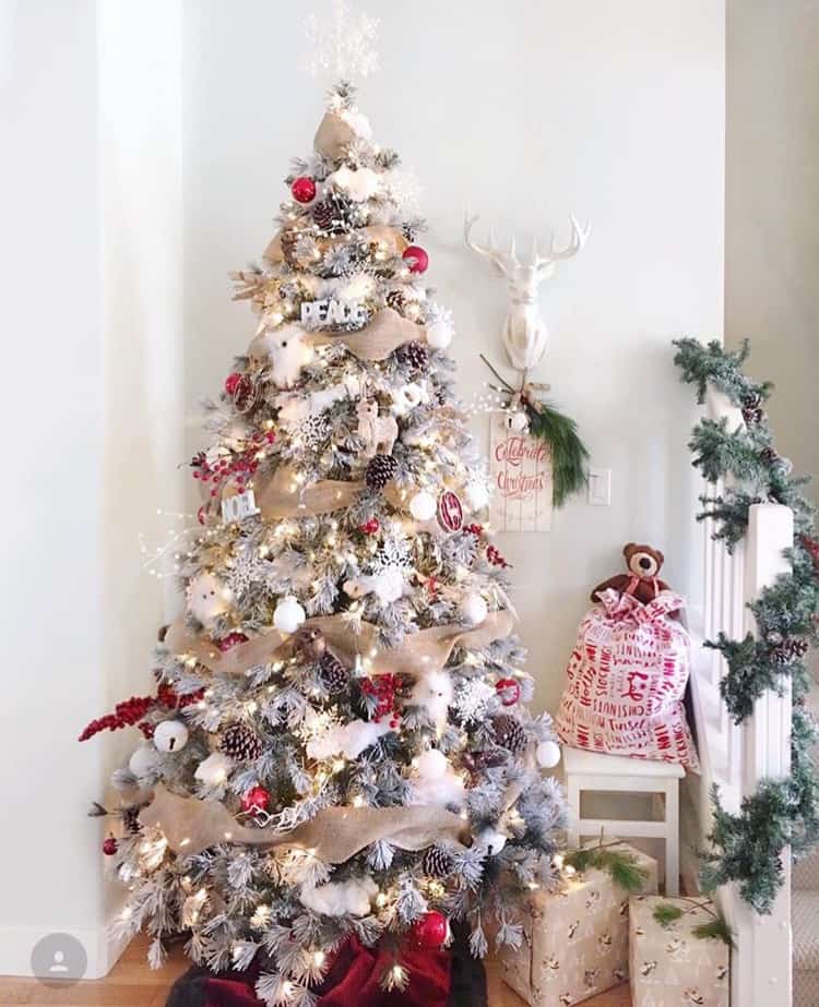 A flocked Christmas tree with burlap ribbon garland and red and white ornaments.
