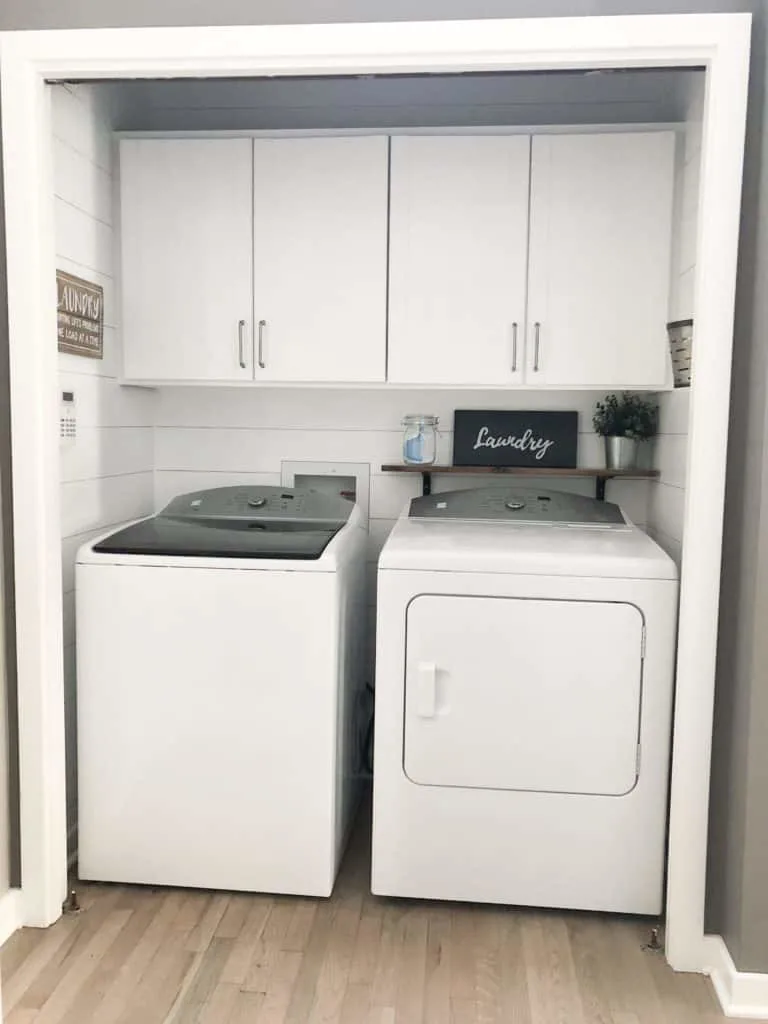 This shows the whole farmhouse style laundry room with the cute galvanized bucked on the wall for lint and a sign that says laundry.