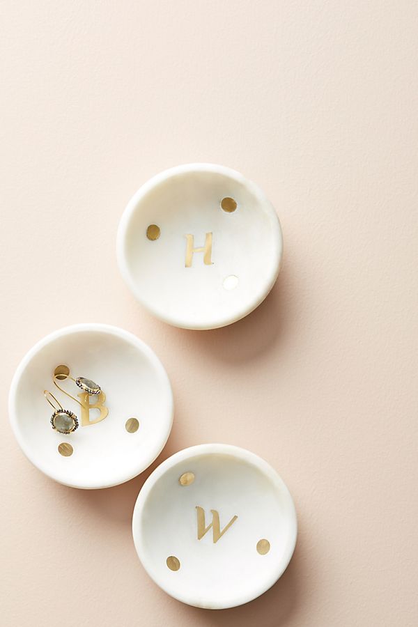 Small white trays with three gold dots and a letter in them.
