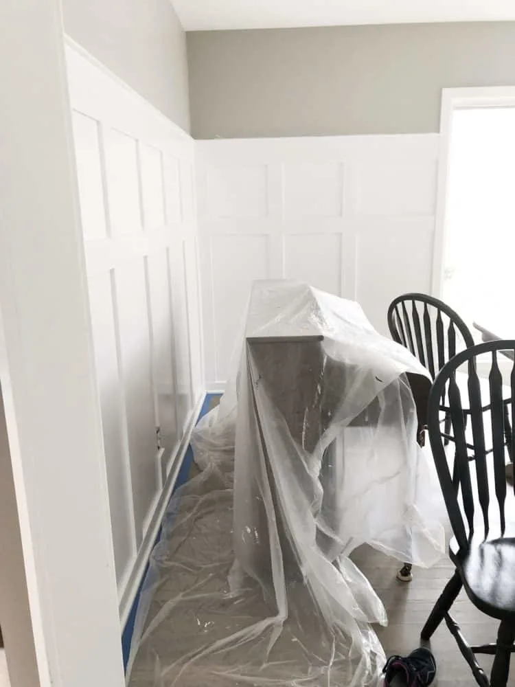 DIY Board and Batten in the process of being painted white with a drop cloth over the piano.