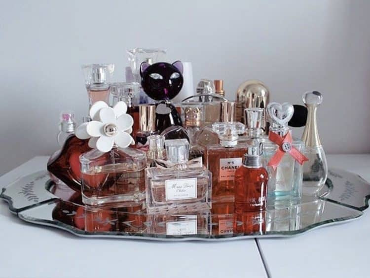 A glass platter with many bottles of perfume of all shapes and sizes.