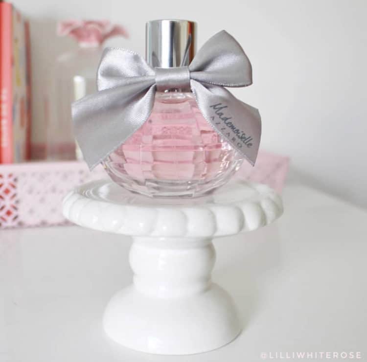 A very small white cake stand with one small pretty bottle of perfume.