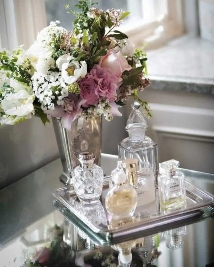 A glass tray with bottles of perfume, a vase with beautiful pink and white flowers.