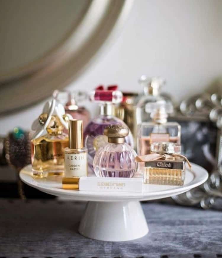 A white cake stand holding beautiful perfume bottles.