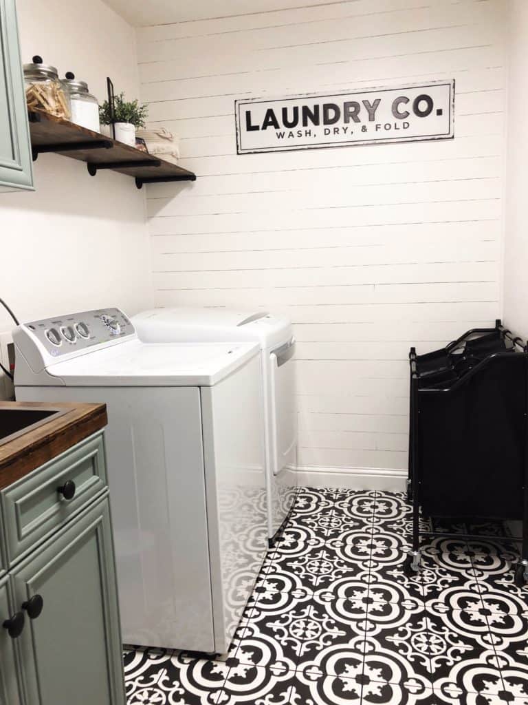 This room has shiplap on the far wall with a laundry co. sign and a wood shelf over the washer and dryer.