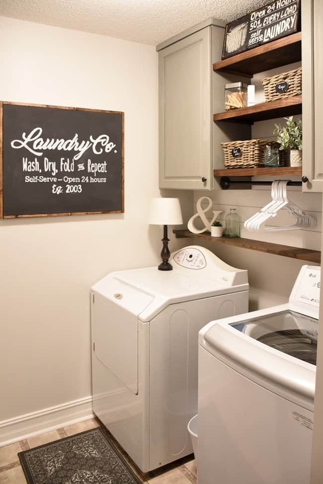 A laundry room with painted cabinets, wood shelves and a laundry co. sign hanging on the wall.