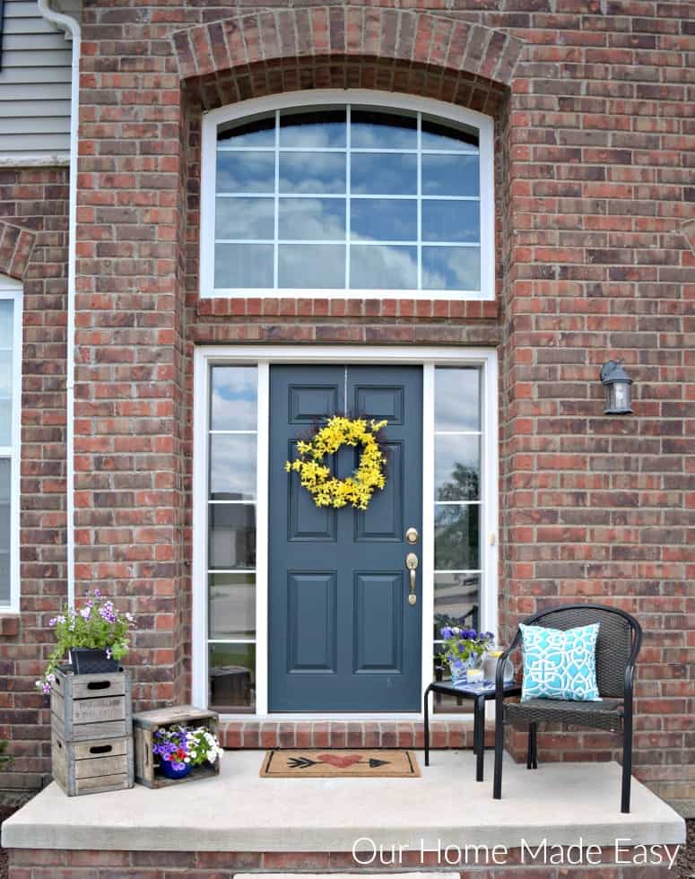 A brick house with a navy front door and yellow flowered wreath.