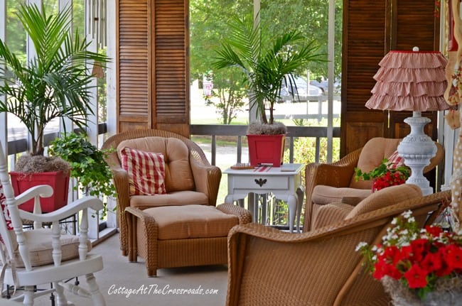 A screened in porch with beige furniture and pops of red in the decor.