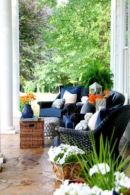 Wicker furniture with navy blue cushions and orange flowers in navy and white pots.