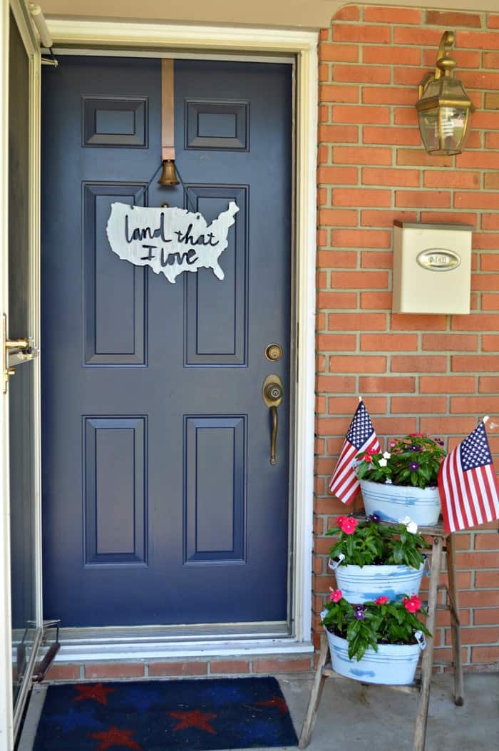 A blue front door with a tiered planter next to it with flags in the top planter.