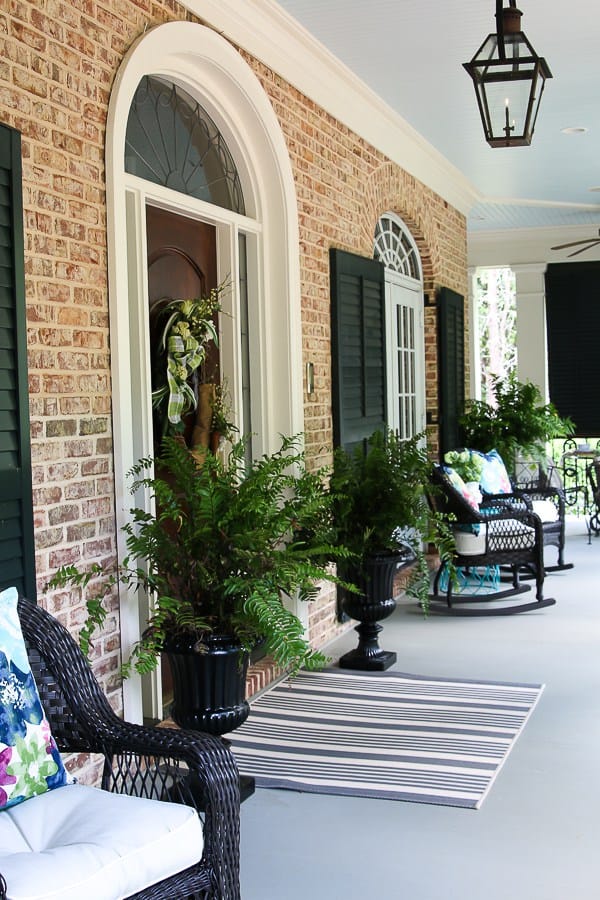 A front porch with black urns that house ferns and rocking chairs. 