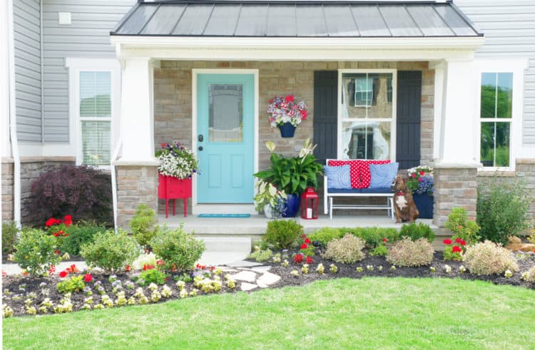 A light blue front door with lots of colorful decor in the pillows, table and pots on the front porch.