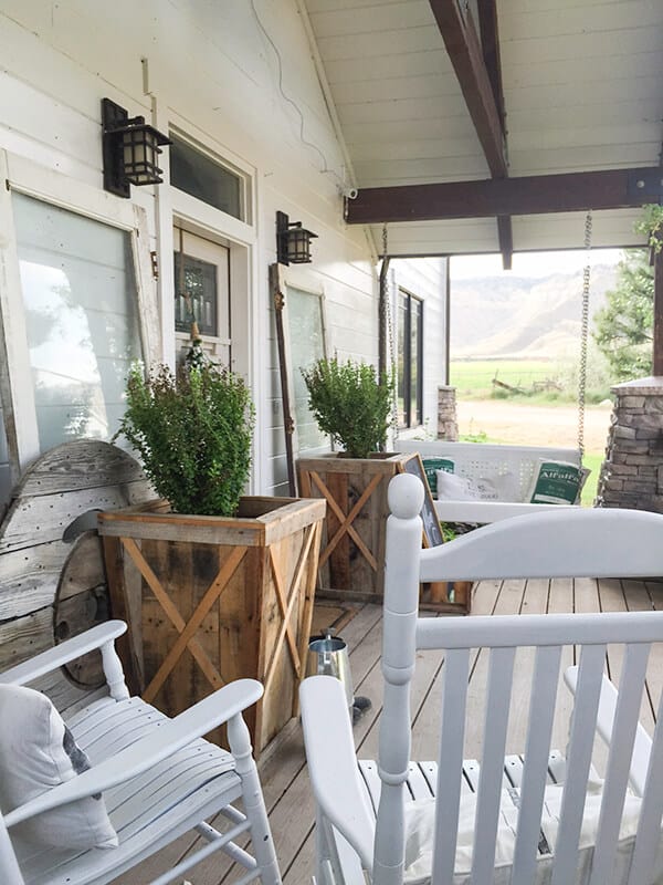 Wooden box planters with boxwood plants in them and white rocking chairs.