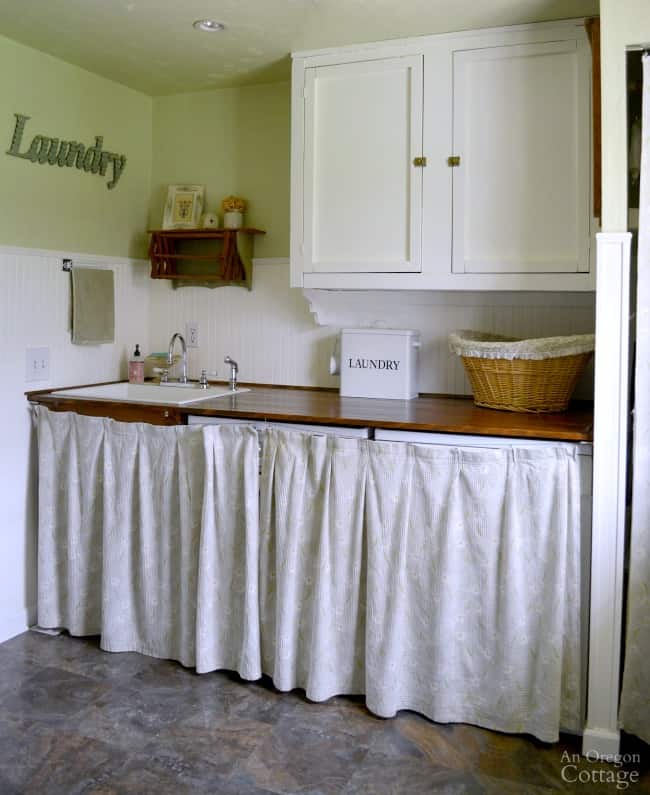 This laundry room has beadboard about 2/3 the way up the walls and green paint on the top 1/3.  There is a wood top over the washer and dryer with a curtain hung in front of it.