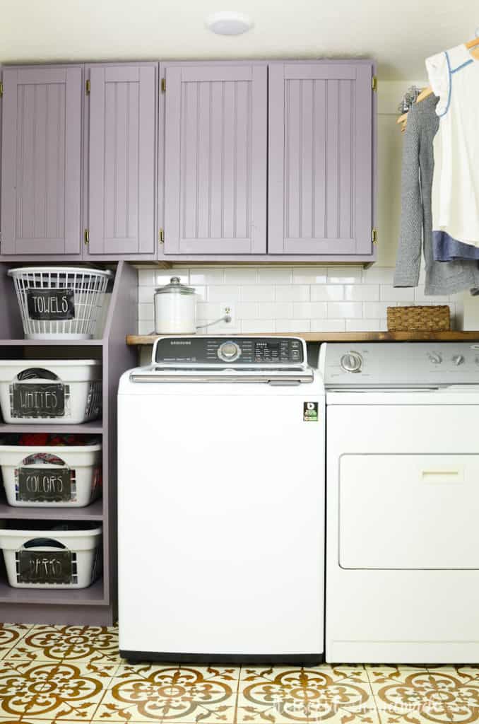 This laundry room has lavender painted cabinetry and subway tile behind the washer/dryer.
