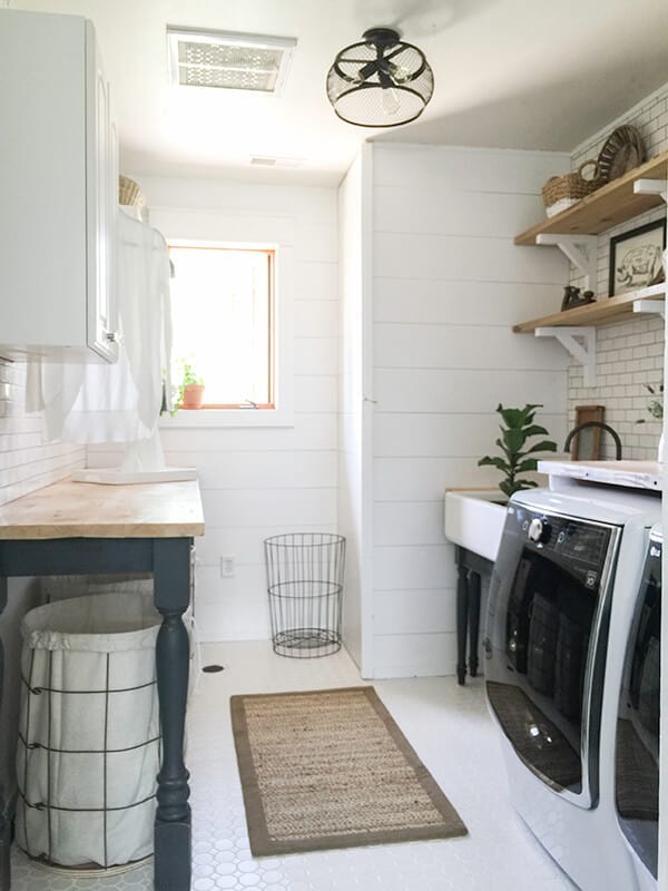 White laundry rom with shiplap and subway tile that has a painted folding table with a wood top.