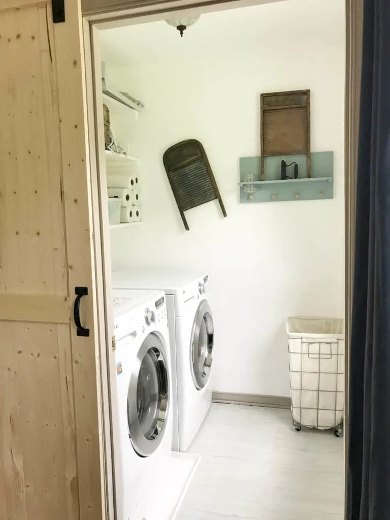 this white laundry room has a large wire laundry basket and old time washboards hung on the wall.