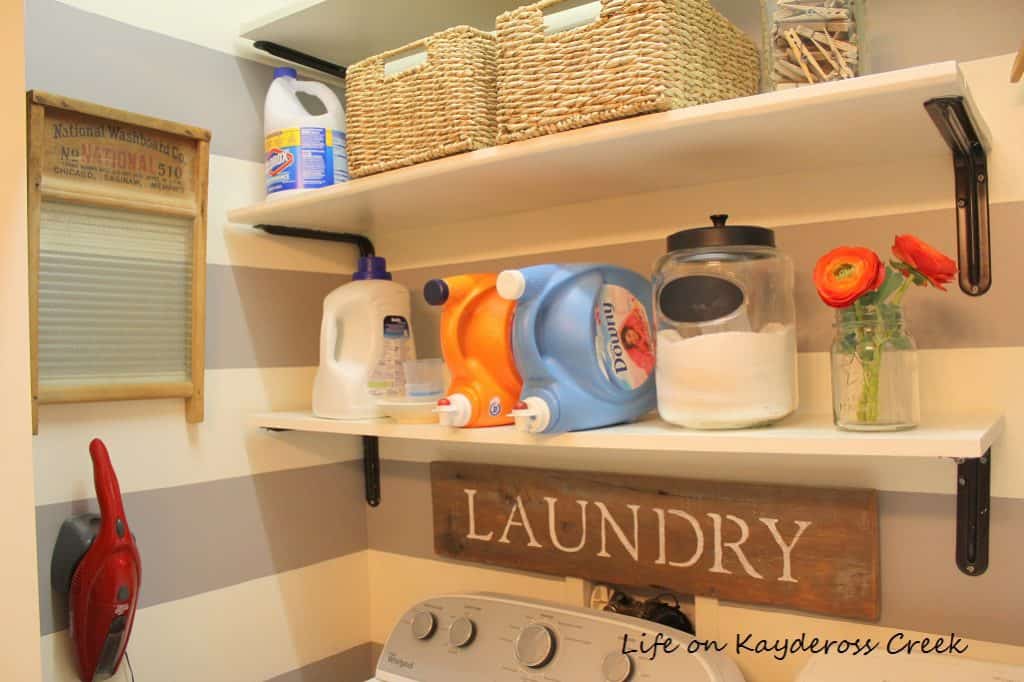This laundry room has gray and white stripes on the wall, white shelving and a laundry farmhouse sign.