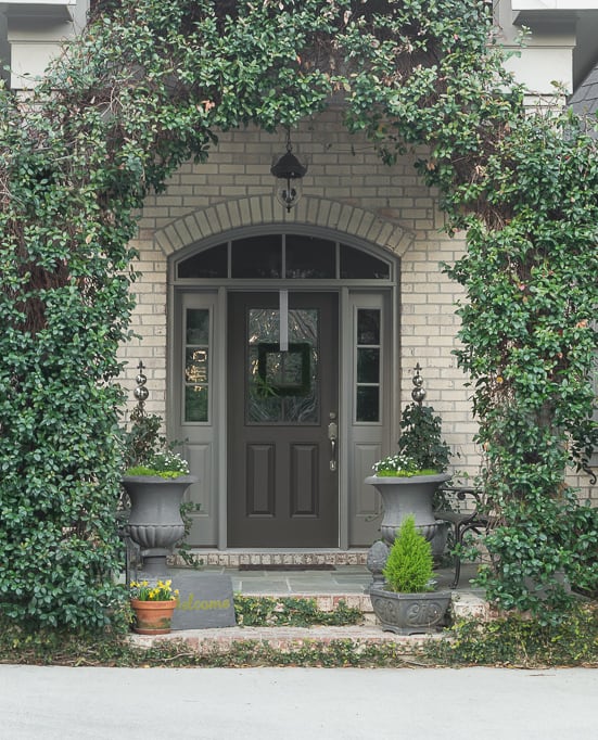 A front door with an arbor leading up to it and lots of greenery.