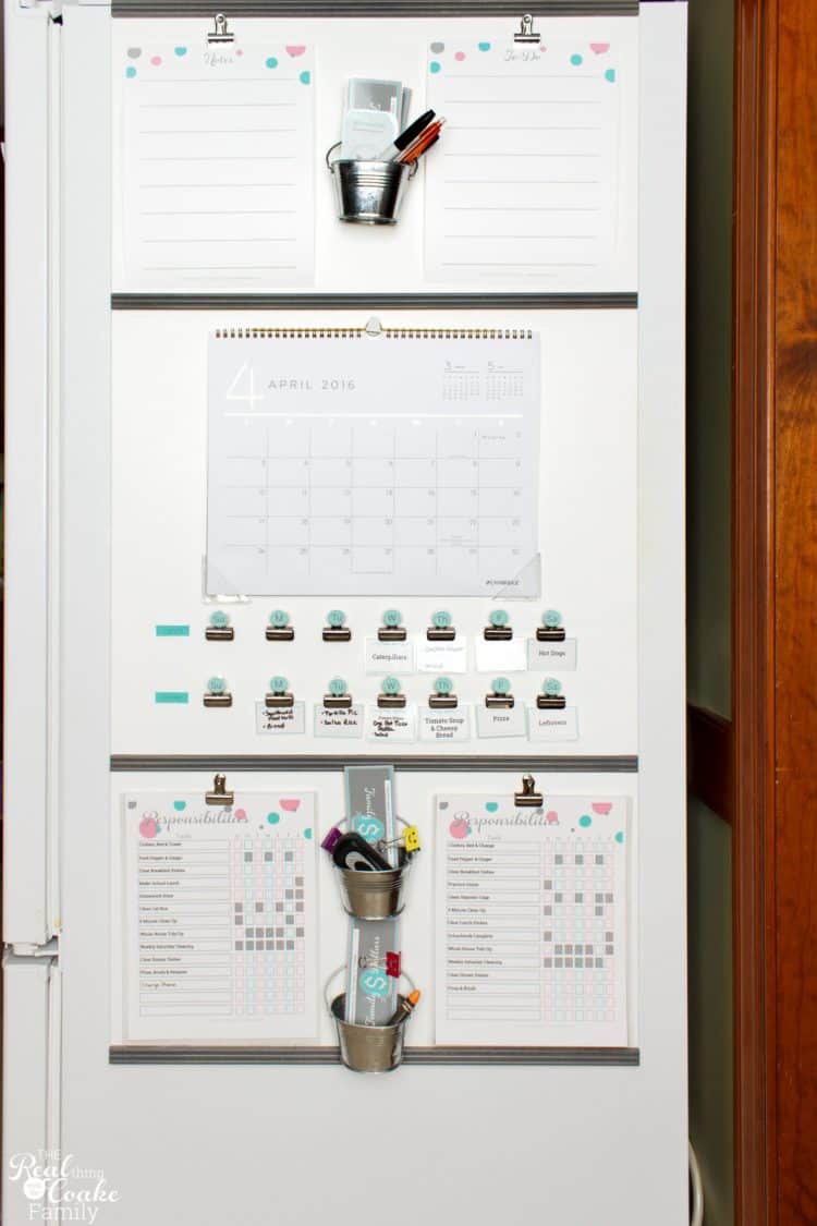 A kitchen command center on the fridge with a large calendar, chore charts and hanging buckets.