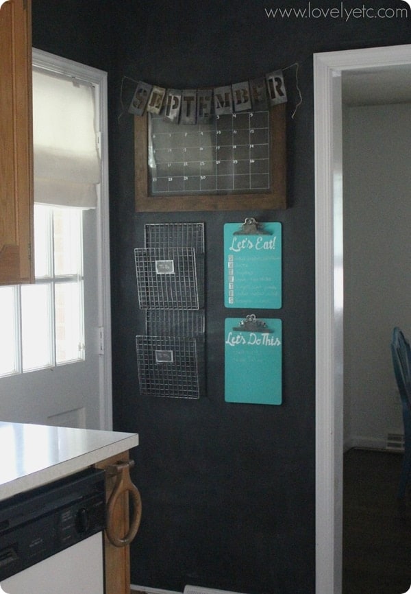A command center on a dark painted wall with a dry erase calendar, to do list, let's eat list and wire baskets for papers.