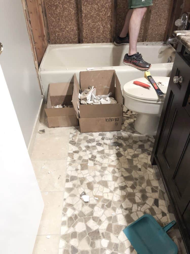 A box on the floor next to the tub which has the tile remnants from demo.