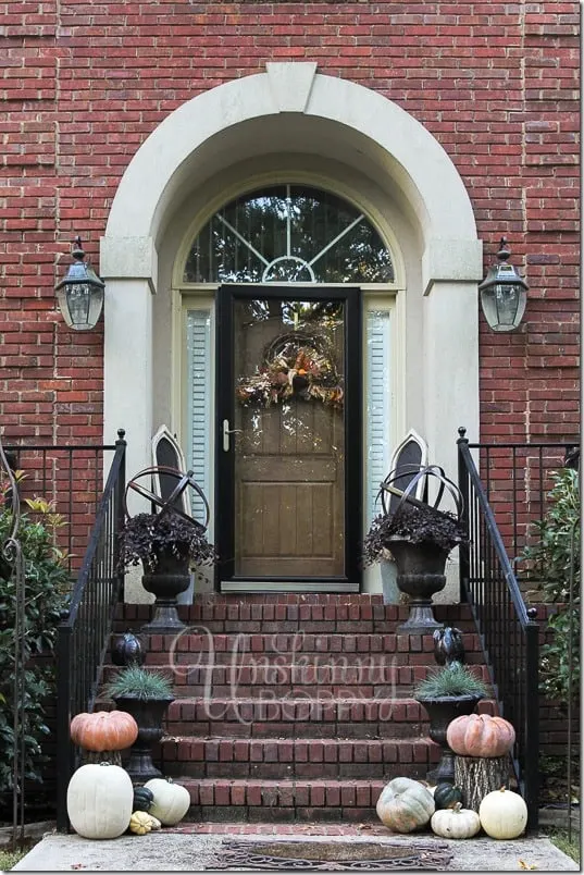 A brick stoop with neutral colored pumpkins sitting on the steps.