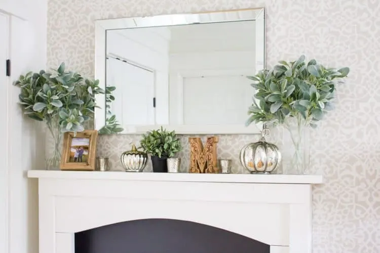 A white fireplace mantel with silver pumpkins on it and lambs ear greenery.