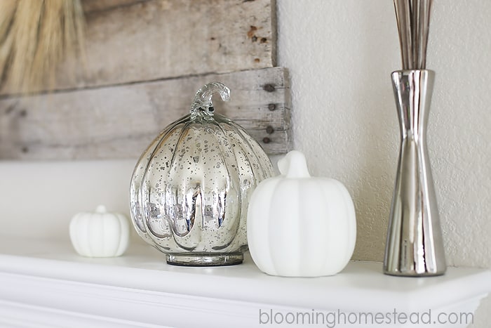 A silver and white pumpkin on a white mantel next to a silver candle stick.