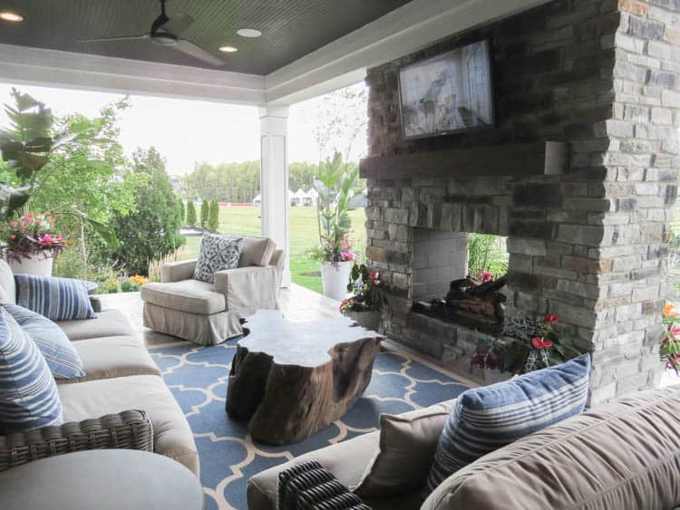 An outdoor relaxing patio that is covered. There are sofas and a fireplace with a tv.