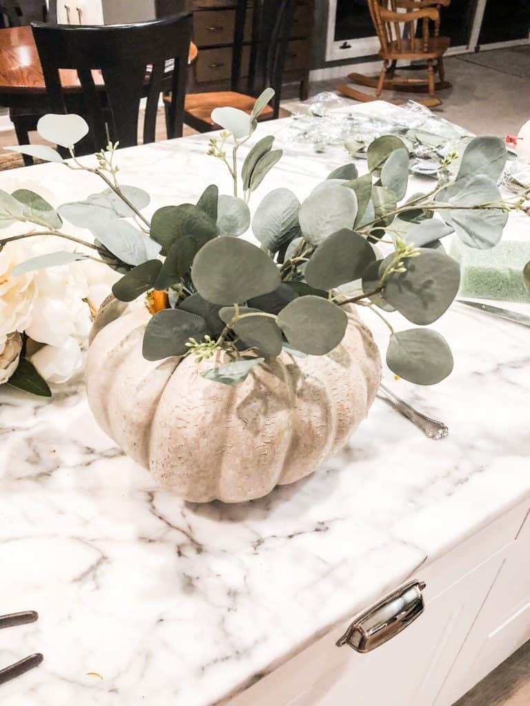 A small pumpkin with fake eucalyptus, the beginning of a flower arrangement.