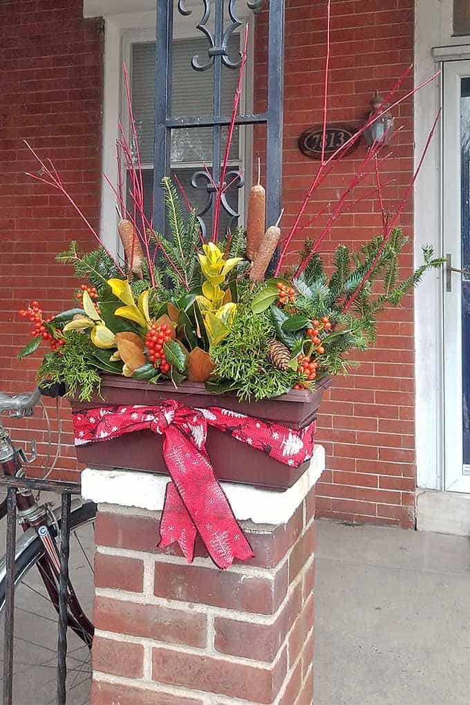 Farmhouse Christmas Decor on a front porch with a planter using christmas greens