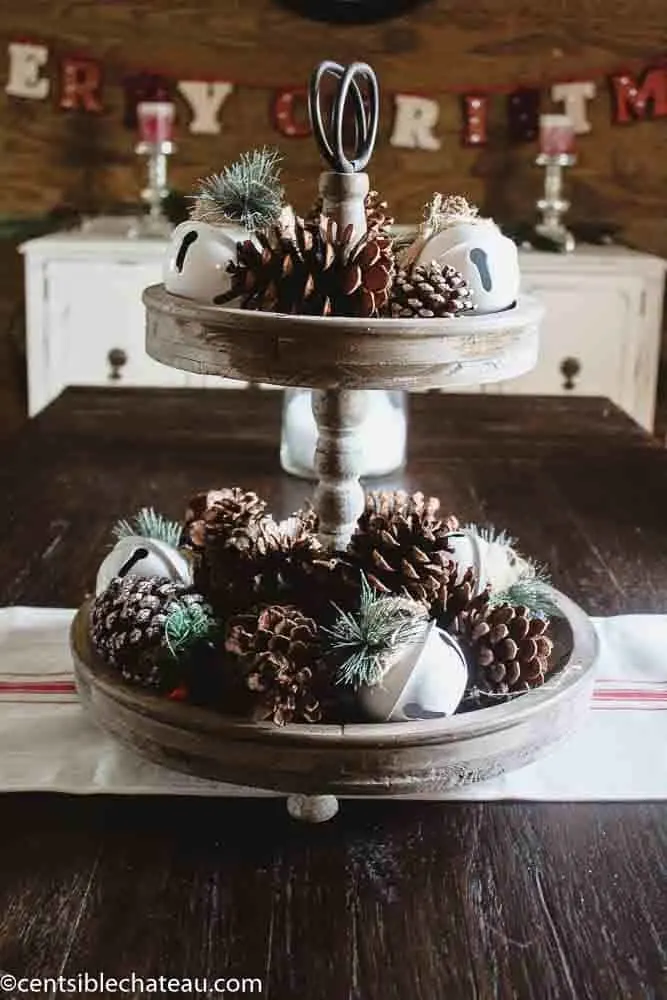 Farmhouse Christmas decor a tiered tray with pinecones and sleigh bells on it.