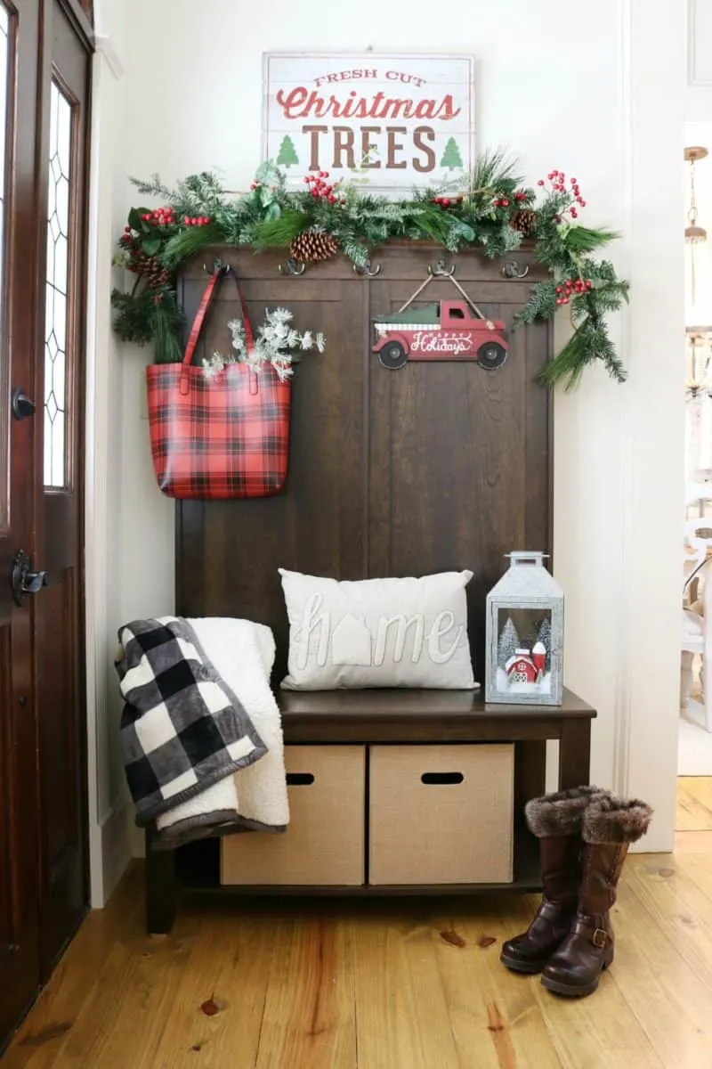 Farmhouse christmas decor front entry with a plaid bag, red truck with christmas tree, garland and christmas trees sign