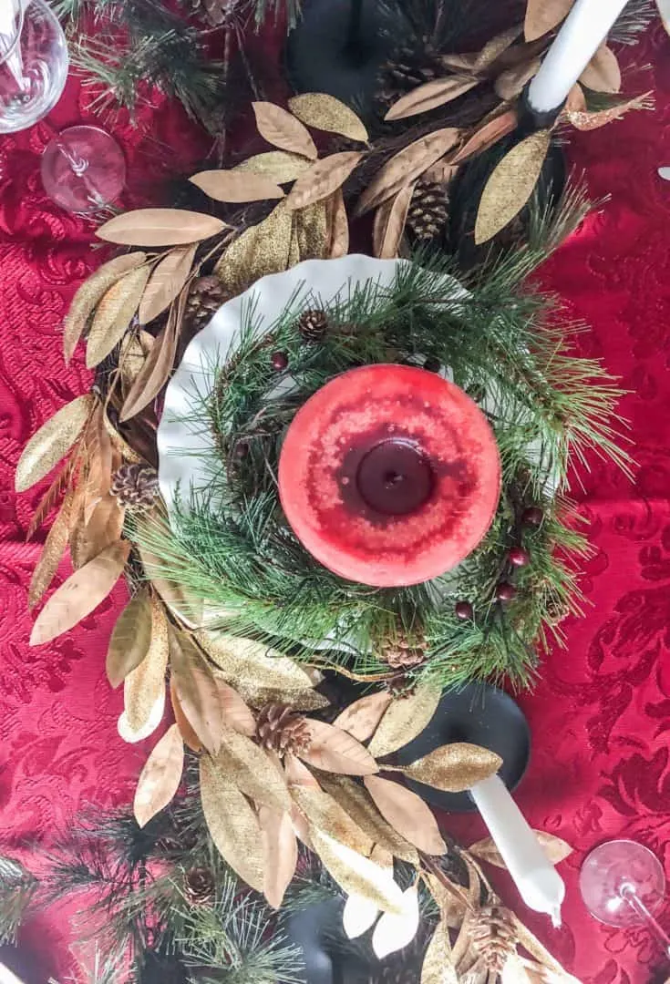 An above view of the centerpiece of a red candle propped up on a white cake plate.