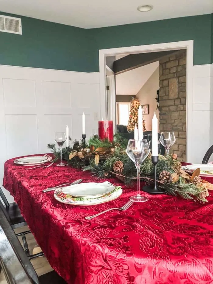 Christmas Table Setting with Red tablecloth, green and gold garland and candles.