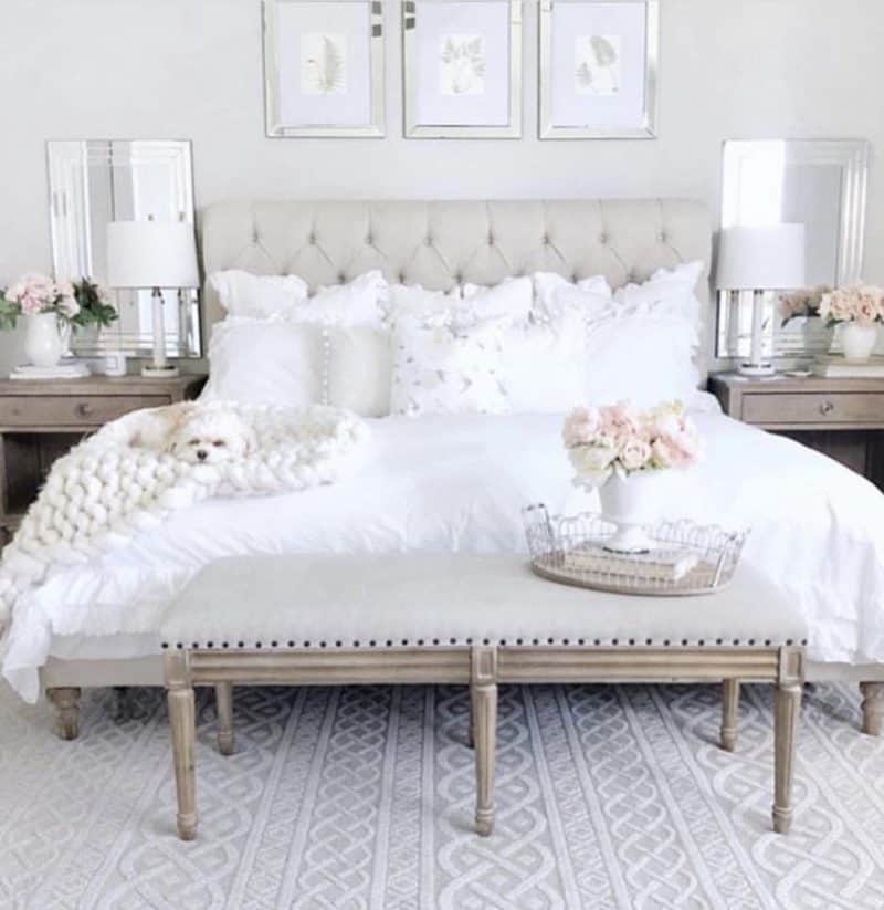This gray tufted headboard has white bedding and a bench at the foot.