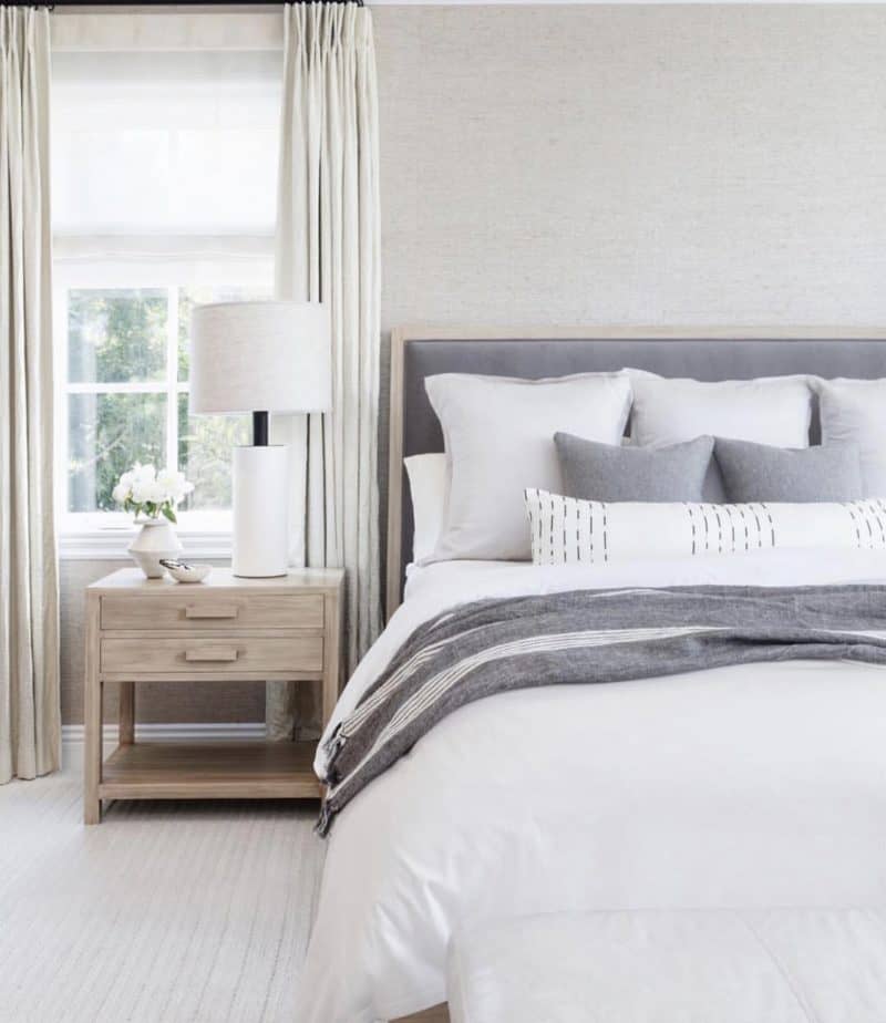 Gray upholstered bed with white bedding and a white lamp for cozy bedroom ideas.