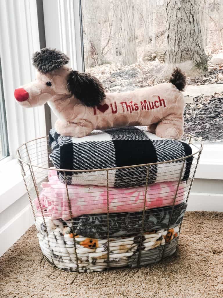 A Gold wire basket full of my daughters blankets with a stuffed animal on top.