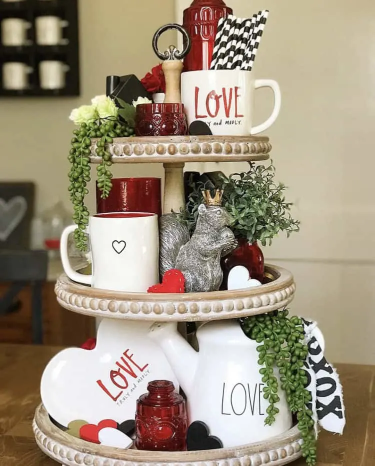 Tiered tray with love written on lots of pottery and some greenery with red accents.
