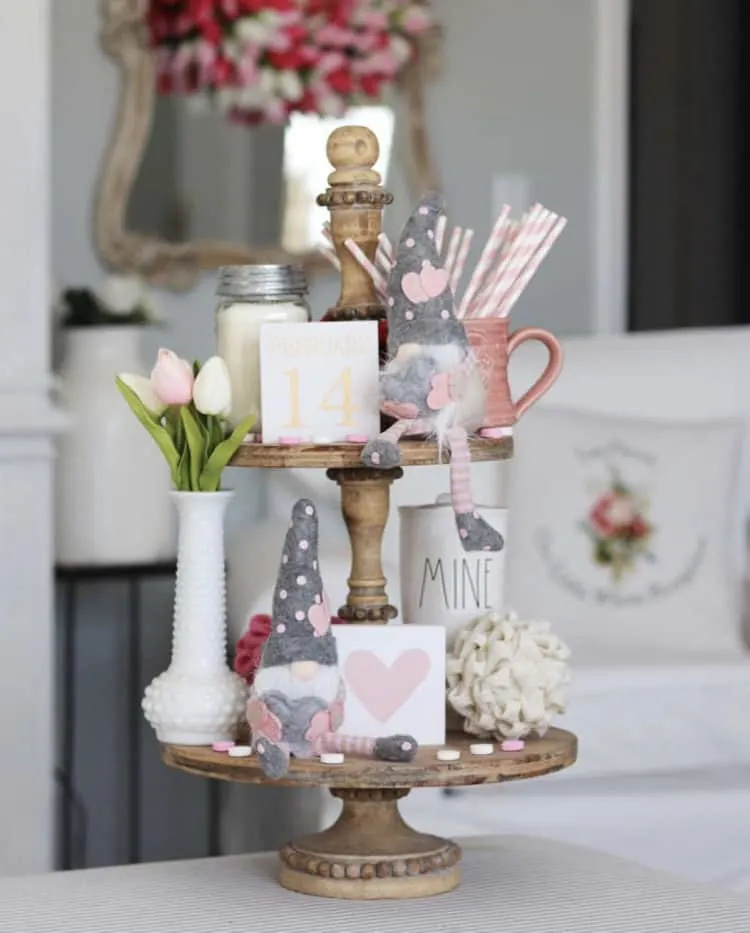 This tiered tray has a milk glass bottle with tulips in it, a couple gnomes with pink hearts on their hats and some bugs that are pink and white.