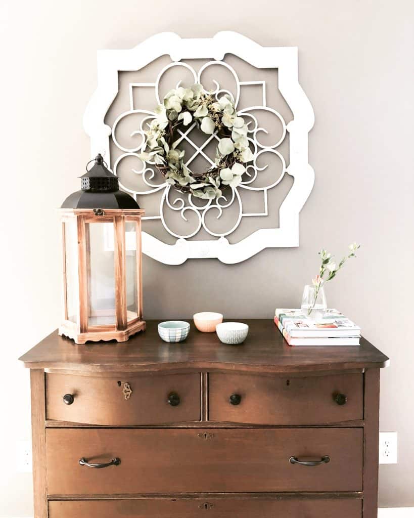 Antique Dresser for storing blankets with a lantern on top, three decorative bowls and a wine glass holding a flower.