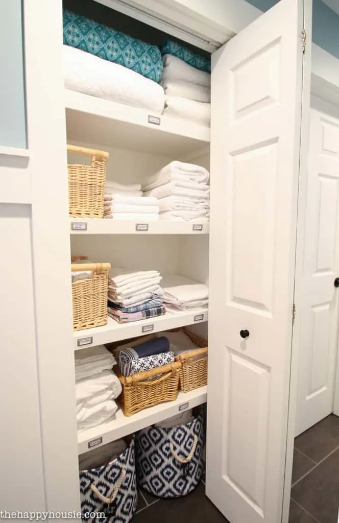 A linen closet with labels on the shelf so everyone knows where everything goes. Towels folded nicely and baskets to corral items.