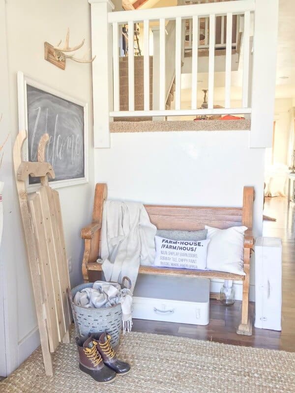 An entryway with white pillows, a white blanket and other neutral decor.