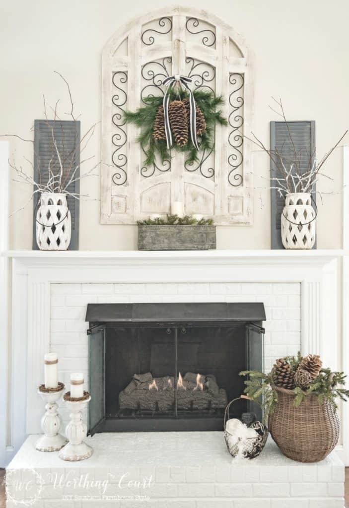 A beautiful mantel with white candlesticks and white candles, white wall decor and white vases.